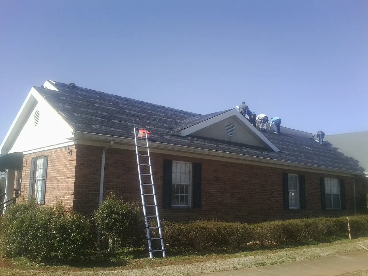 Crew tearing shingles off a brick ranch roof with a ladder set — Emergency Roof Repair work by our crew in Sanborn