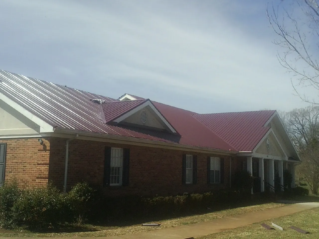 Red metal roof with gabled entries on a long brick building, from a Hail Damage Roof Repair job in Sanborn