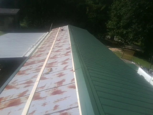 Old rusted panels beside newly installed green metal roofing — Wind Damage Roof Repair by Roofing Brothers in Sanborn
