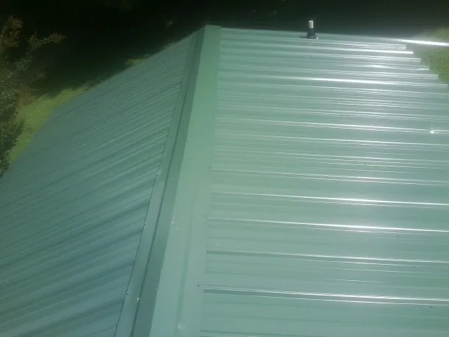 New green metal panels meeting at the ridge of a roof — Flat Roof Repair work by our crew in Sanborn
