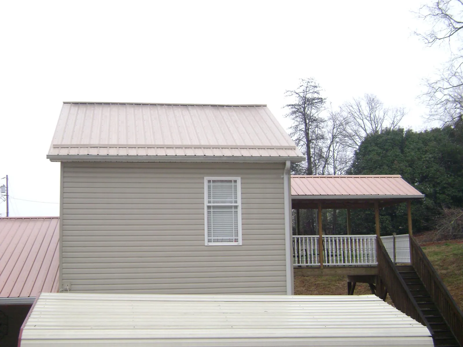 Tan metal roofs on a two story addition and attached porch, from a Roof Replacement job in Sanborn